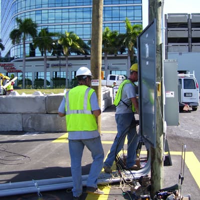 Two Rayco Electric technicians in high-visibility vests working on a commercial electrical panel